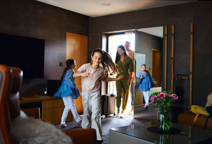 A cheerful young family with two kids entering a room at a luxury hotel during their summer vacation.