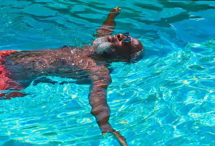 A mature man is leisurely floating on his back in a pool, enjoying the relaxation.