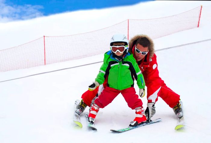 A man helping a child navigate down a ski slope.