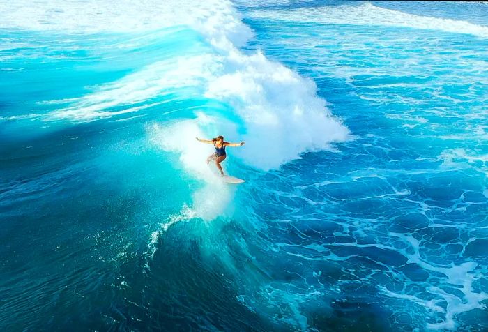 A woman surfing the enormous waves of a sparkling turquoise sea.