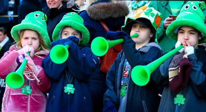 A group of young children in bright green hats blow into green plastic horns during Boston’s St. Patrick's Day parade.