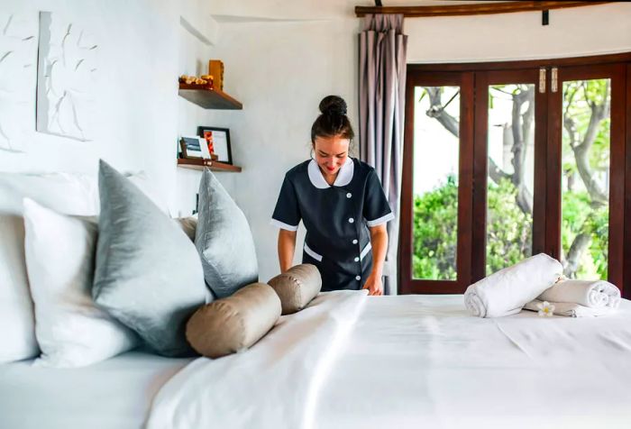 A hotel maid in a uniform with her hair styled in a bun, making the bed.