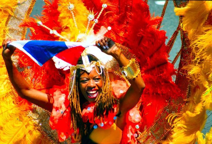 A joyful dark-skinned woman dons a colorful feathered backpack wing, smiling brightly as she holds a piece of clothing during the festivities.