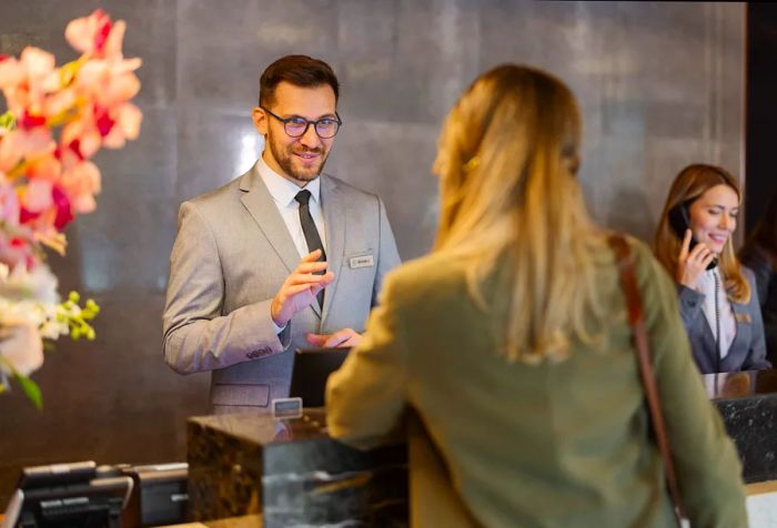 A male receptionist engages in conversation with a hotel guest at the front desk.