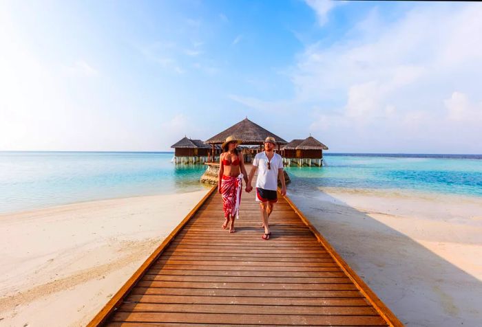 A charming couple strolling hand in hand along the boardwalk towards the beach.