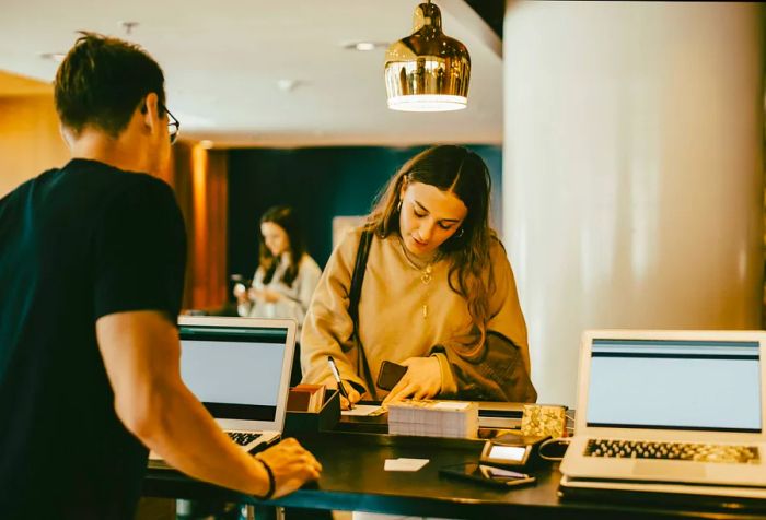 A young woman is completing a form at the front desk while the man behind the counter reviews it.