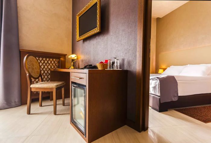 A hotel room featuring a dark wood desk partitioned from a spacious bed dressed in crisp linens.