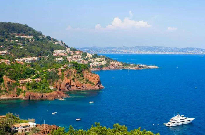 A luxurious yacht glides over azure waters, with the stunning bay beach and Cannes in the background ©rochus/Shutterstock