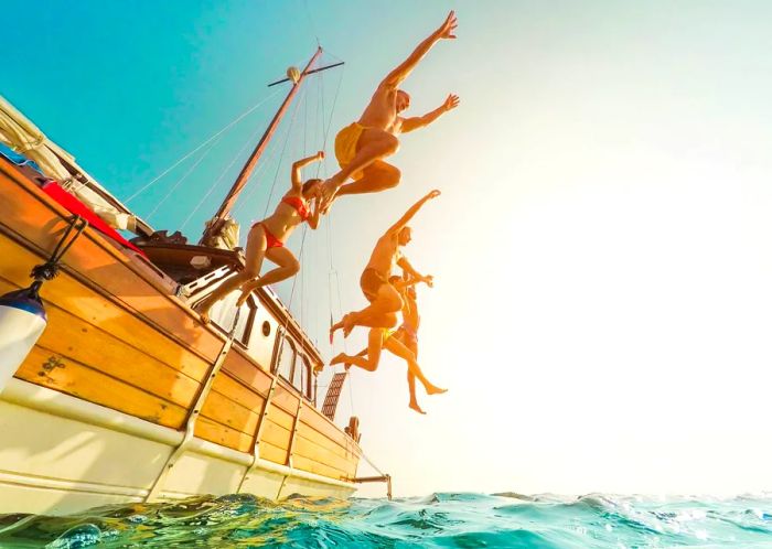 Five individuals leaping from a sailboat into the ocean during summer ©DisobeyArt/Getty Images