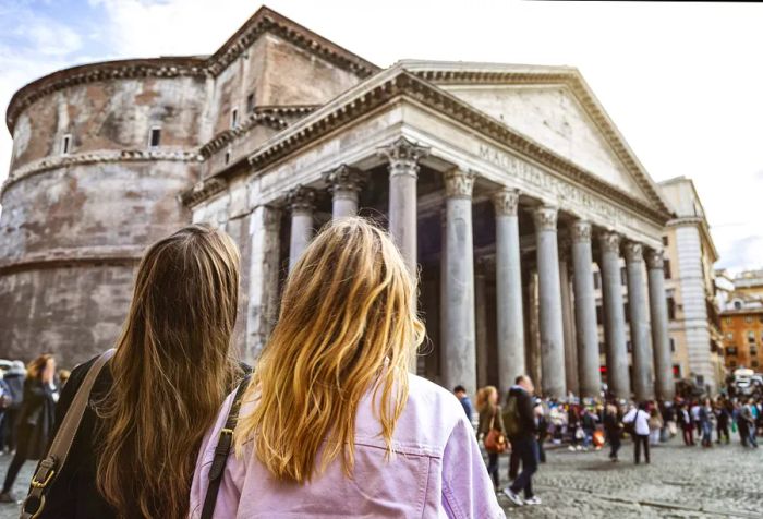 Two women gaze towards the Pantheon, watching the passersby across the piazza.