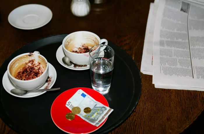 Visual of untouched coffee cups and a newspaper on a café table with a tip in EU currency