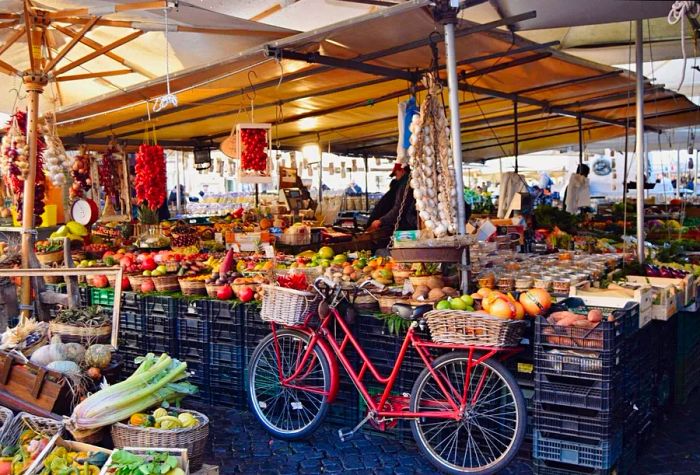 A tent showcasing a variety of fruits for sale, next to a bicycle laden with baskets full of goods.