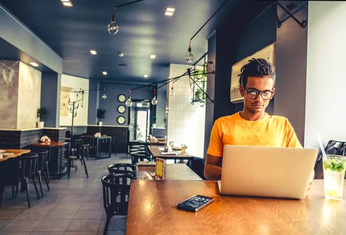 A solitary man diligently works on his laptop at a café.