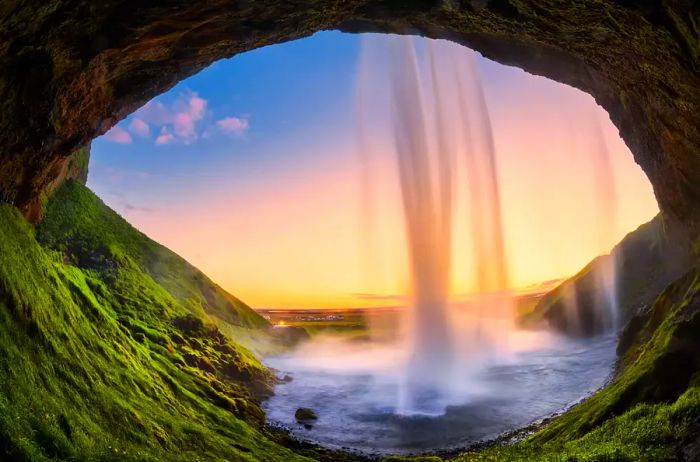 A view from behind the Seljalandsfoss waterfall in Iceland at sunset.