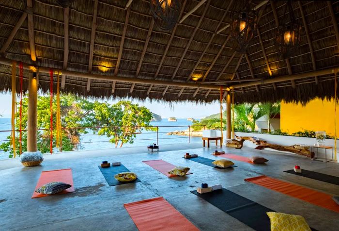 An open yoga studio with a thatched roof, offering a stunning view of the sea.