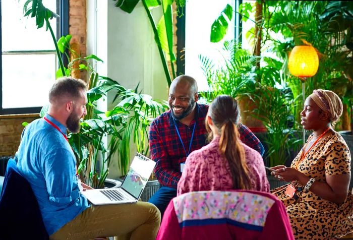 An amputee conducts a meeting with three colleagues inside a café surrounded by lush greenery.