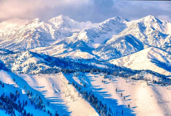 A picturesque view of rugged ski terrain surrounded by frosted tall trees and steep, snow-covered mountains.