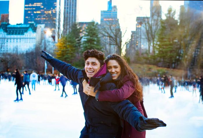 A young woman embraces her partner from behind while they enjoy ice skating outdoors.