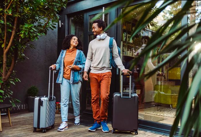 A young couple at the entrance of a building with their luggage.