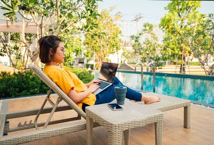 A young woman lounging by the pool with her laptop on her lap.