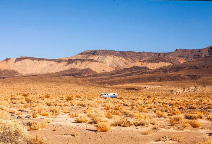 A camper van traversing a desert landscape with mountains visible in the distance.