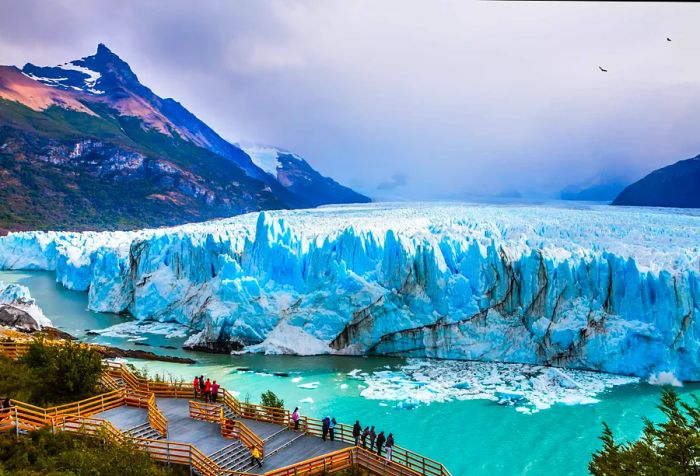 Visitors on a boardwalk observing a glacier as it slowly melts into a lake.