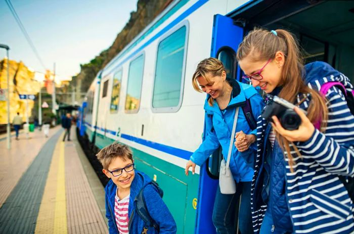 A mother and her two children disembark from a train at an Italian station