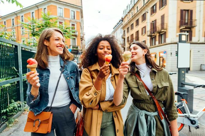 Three joyful women enjoying ice cream while strolling through an Italian city and sharing laughter