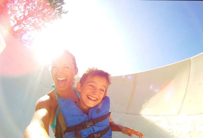 A woman and child in a life jacket smile as they glide down a water slide.