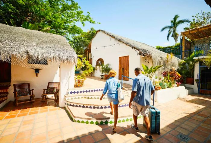 A couple traversing the tiled floor of a resort, dragging their luggage behind them.