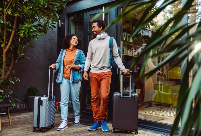 A young couple with their suitcases standing at the entrance of a building.