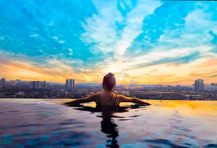 A woman is seen from behind, standing at the edge of an infinity pool, overlooking a city skyline against a dramatic sky.