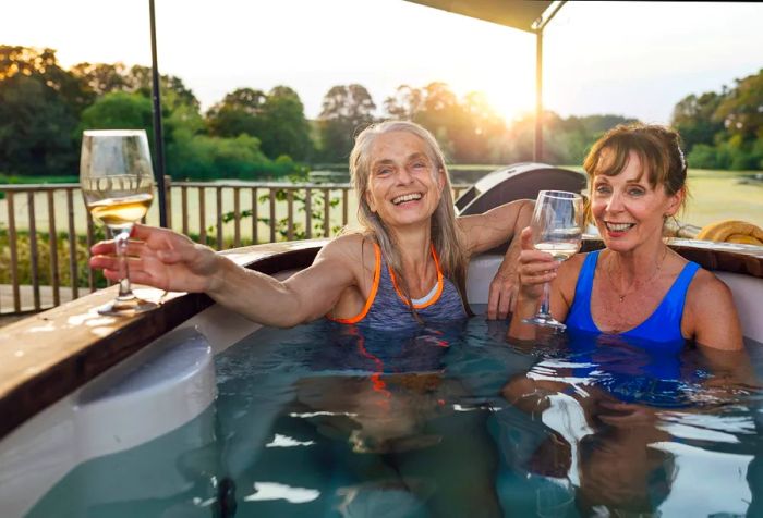 Two women enjoying wine while relaxing in a hot tub.