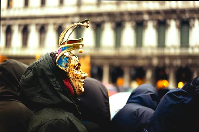 A man adorned with a Venetian mask amidst a crowd during the Venice Carnival