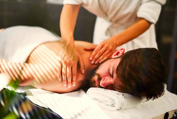 A bearded man relaxes on a massage table while receiving a back massage.