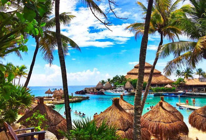 A group of tourists enjoys a small beach surrounded by thatch umbrellas.