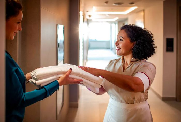 A close-up of a maid replacing towels for a young woman staying at the hotel.