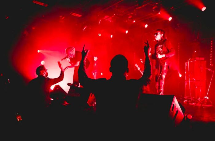 Performers engage with the audience on stage under red spotlighting.