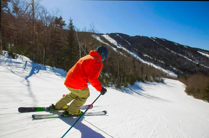 A skier clad in a bright orange jacket glides down the snowy slopes