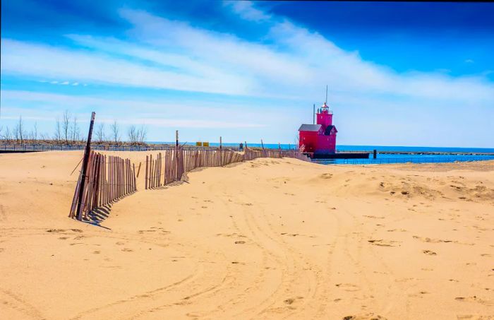 An expansive sandy beach bordered by a fence, with a prominent red lighthouse visible in the distance.