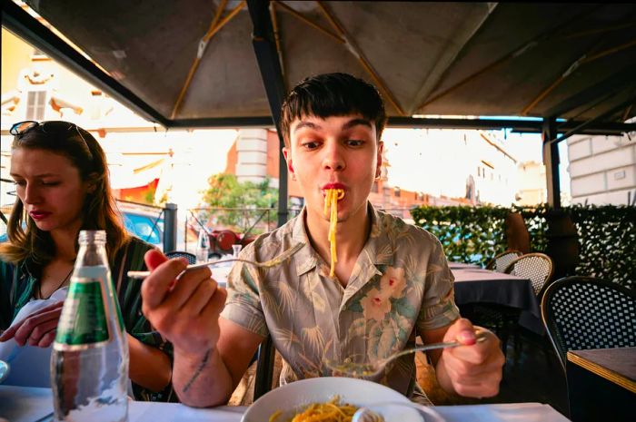 A front-view image of a young man savoring a delicious meal in Italy, dressed casually.