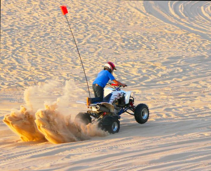 A quad rider performing a burnout on the sandy terrain in Michigan