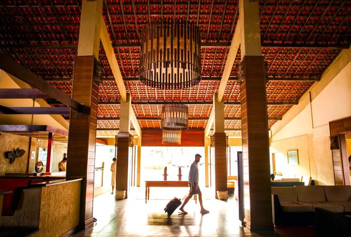 A man strolls through a hotel lobby while pulling his luggage behind him.