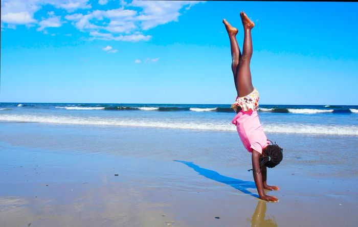 A girl performing a handstand on a beach in Maine