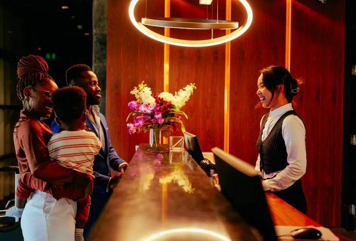 A joyful couple, accompanied by their young son, stands at the hotel reception, where a clerk warmly welcomes them and assists with the check-in process.