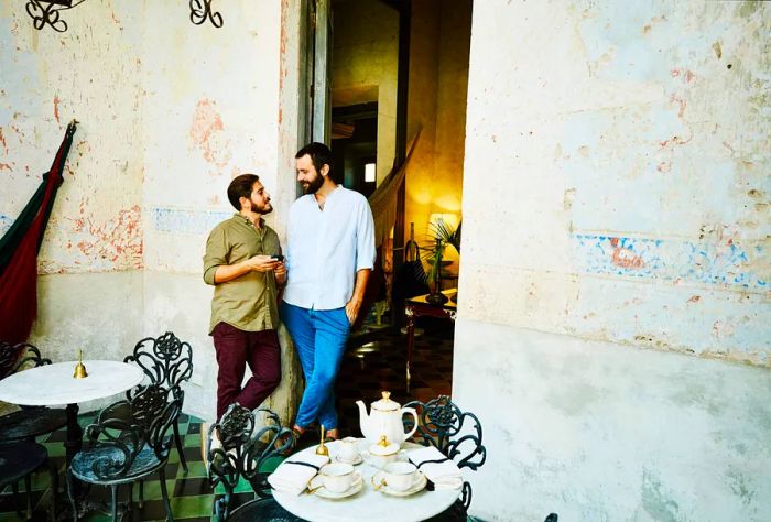 A same-sex couple enjoys a moment leaning against the wall of an outdoor café.