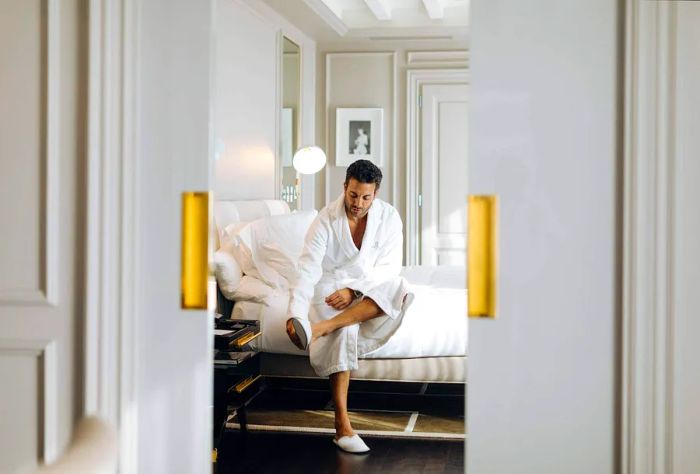 A man dressed in a white robe relaxes in the bed of an opulent suite.