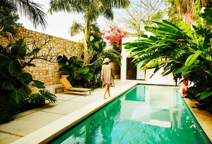 A woman leisurely walks along the edge of a serene pool, with a wall surrounding the area to provide a sense of privacy and seclusion within the beautiful setting.