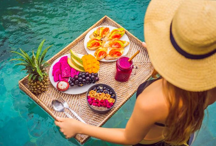 A woman carries a food tray overflowing with fruits as she heads towards the swimming pool.