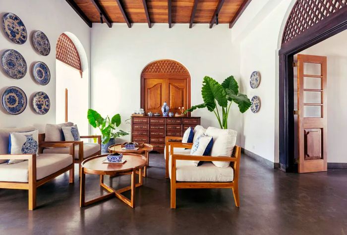 A bright and airy living space featuring seating, wooden coffee tables, potted plants, and decorative wall plates.